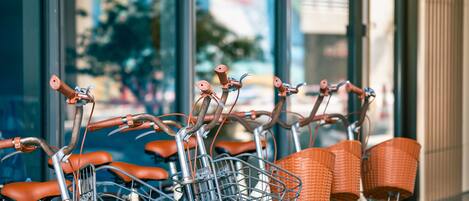 A row of bicycles with baskets and orange seats parked in front of a building with large windows.