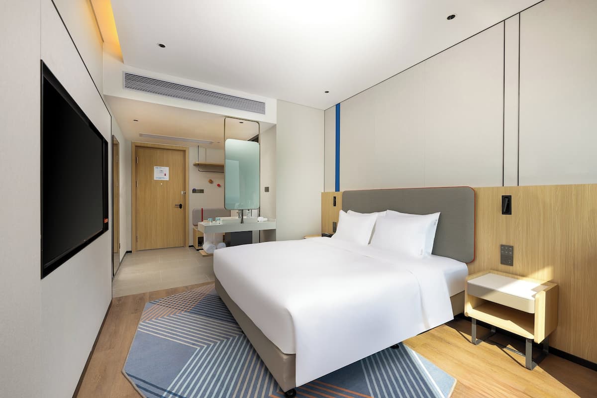 Una habitación de hotel moderna con una cama grande, mesita de noche y televisor montado en la pared.