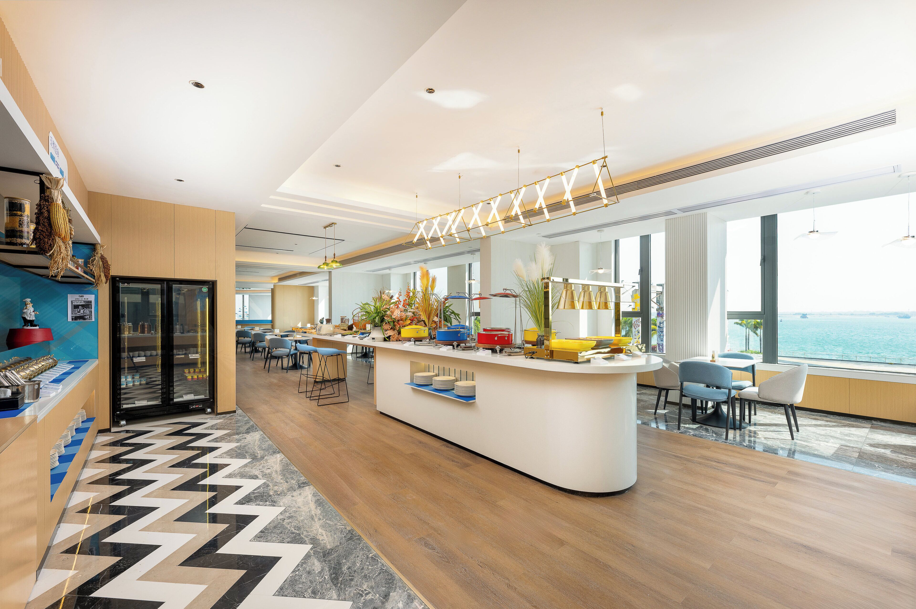 Un hall d’hôtel moderne doté d’un comptoir d’accueil central, d’un espace salon et de grandes fenêtres offrant une vue sur la mer.