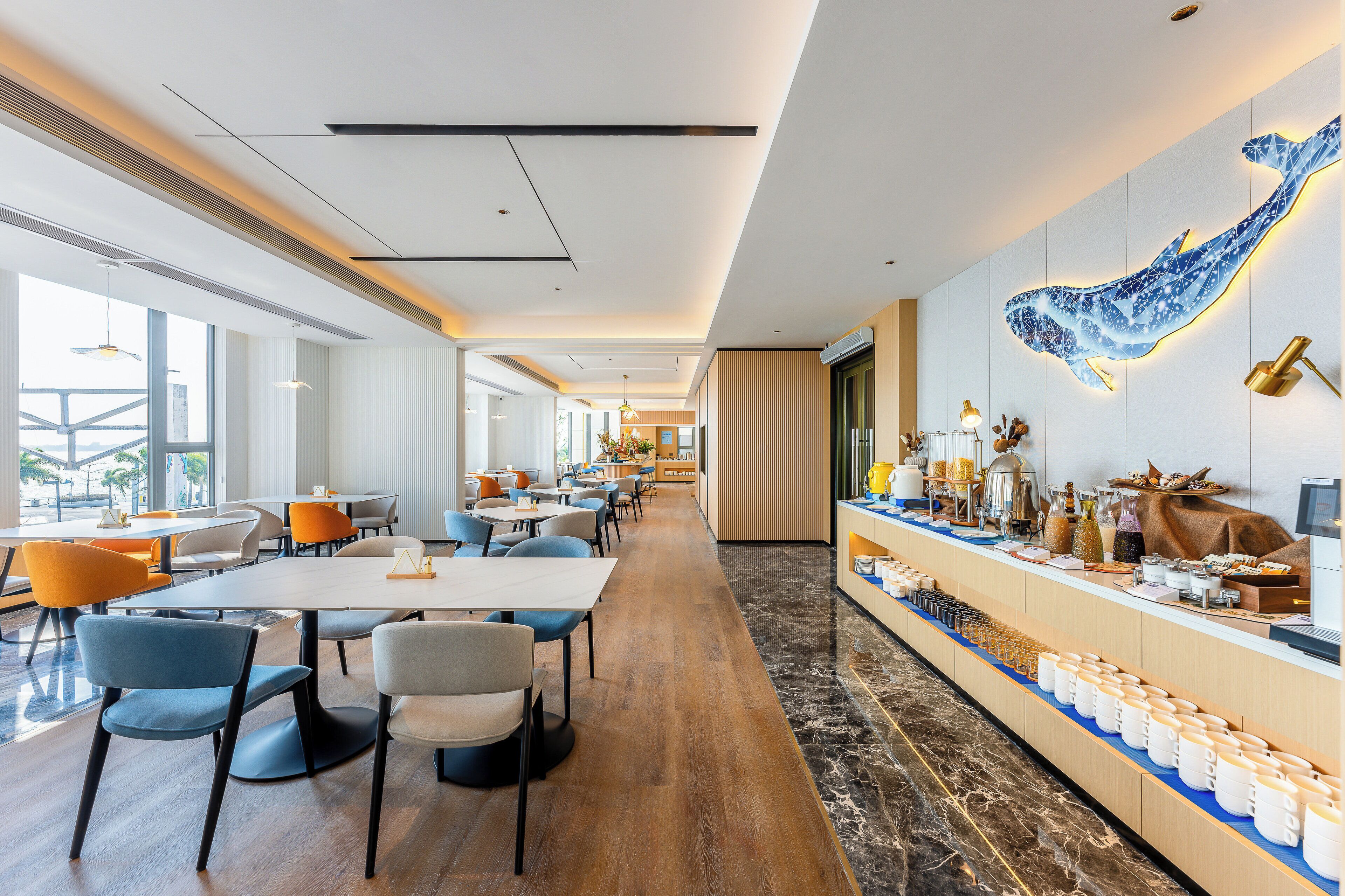 A modern hotel lobby with a long reception desk, seating area, and a large wall mural.