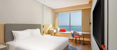 Una habitación de hotel moderna con una cama grande, un escritorio, una silla y una ventana con vistas al mar.