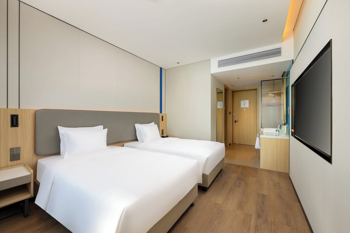 Habitación de hotel con dos camas, un escritorio, baño con espejo y televisor.