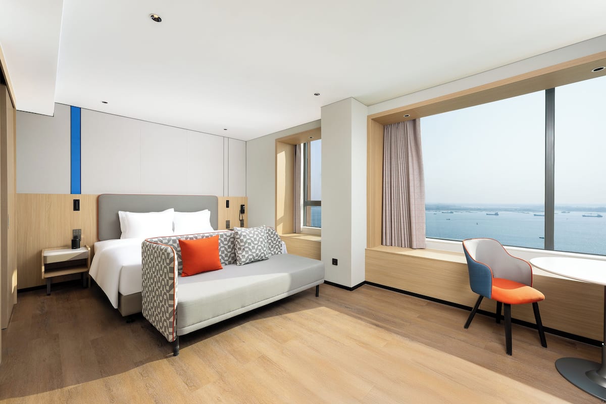Una habitación de hotel moderna con cama, escritorio y vista al mar.