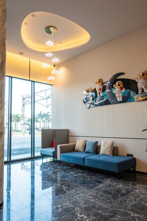 A modern lobby with a blue sofa, a large artwork of astronauts on a moon, and a ceiling with circular lights. - Holiday Inn Express Zhanjiang Coast by IHG (Zhanjiang)