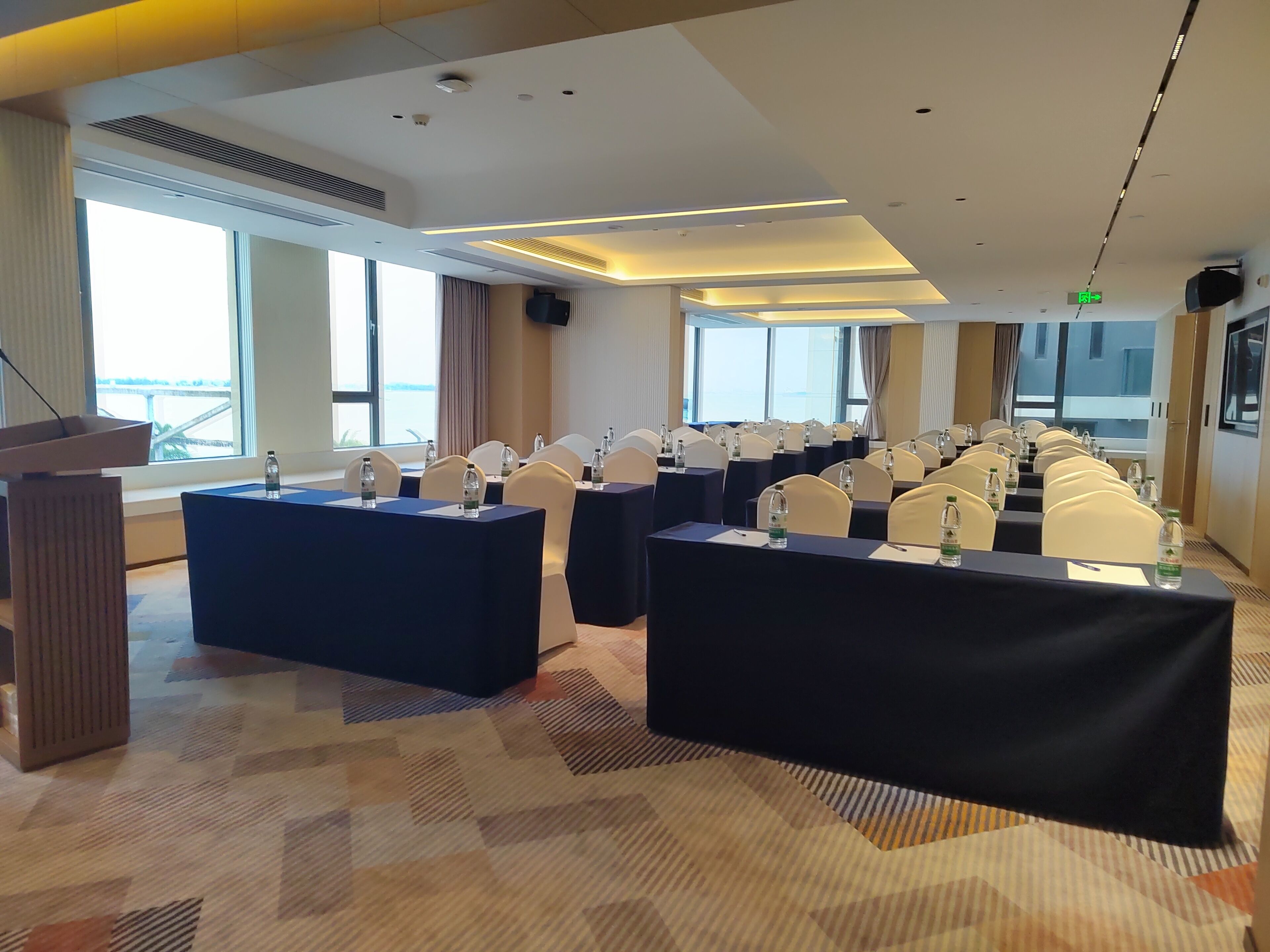 Een vergaderzaal met meerdere tafels, stoelen en een spreekgestoelte.
