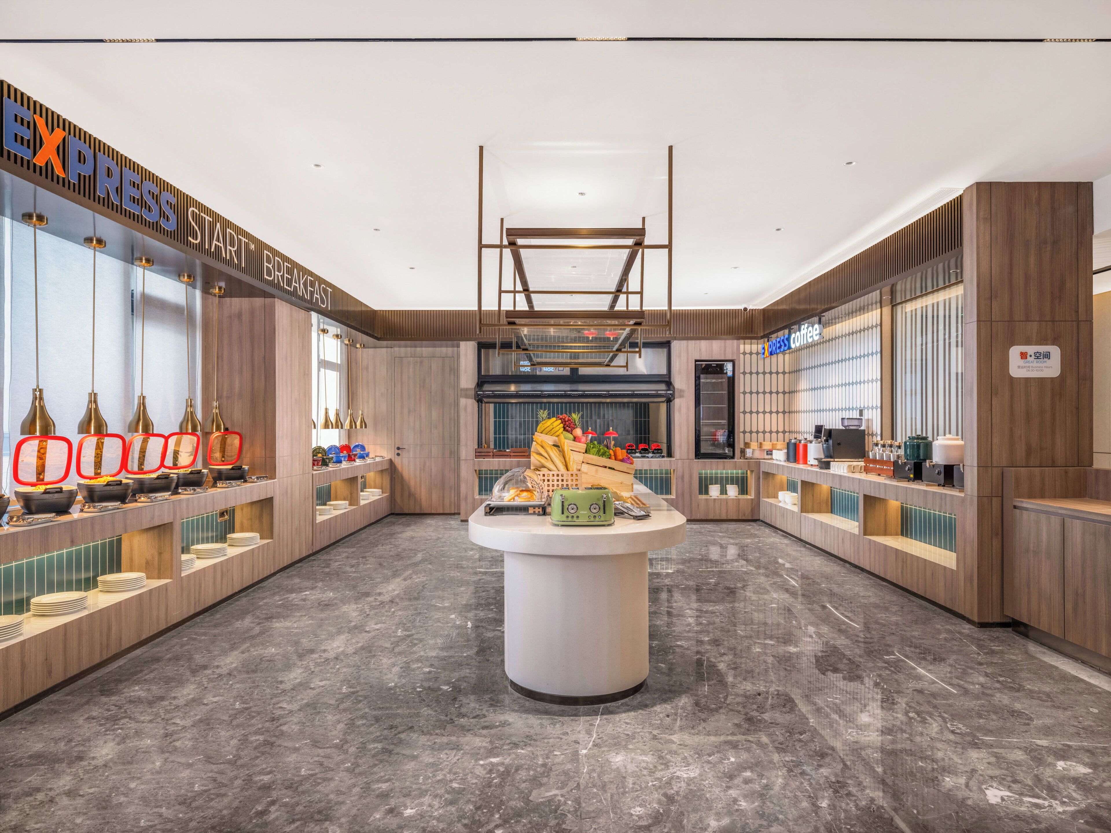 A modern hotel lobby with a central island, breakfast bar, and coffee station.