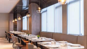 A modern dining area with long tables, chairs, and pendant lighting.