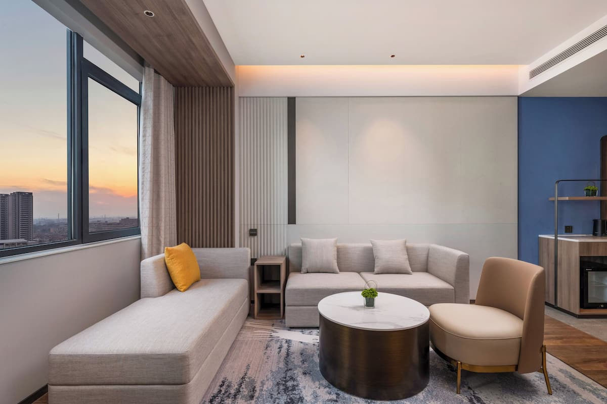 A modern living room with a sofa, armchair, and coffee table, a view of the cityscape through large windows, and a blue accent wall.