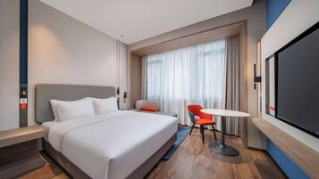 Een moderne hotelkamer met een groot bed, een bureau, een stoel, een televisie en een raam met gordijnen.