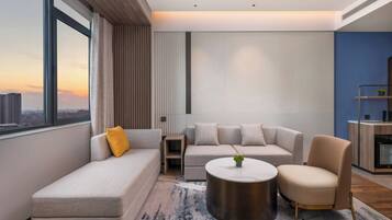 Un salón moderno con sofá, sillón y mesa de centro, vista panorámica de la ciudad a través de ventanas amplias, y una pared decorada en azul.