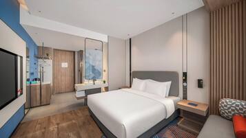 A modern hotel room with a large bed, a TV, a desk, and a seating area.