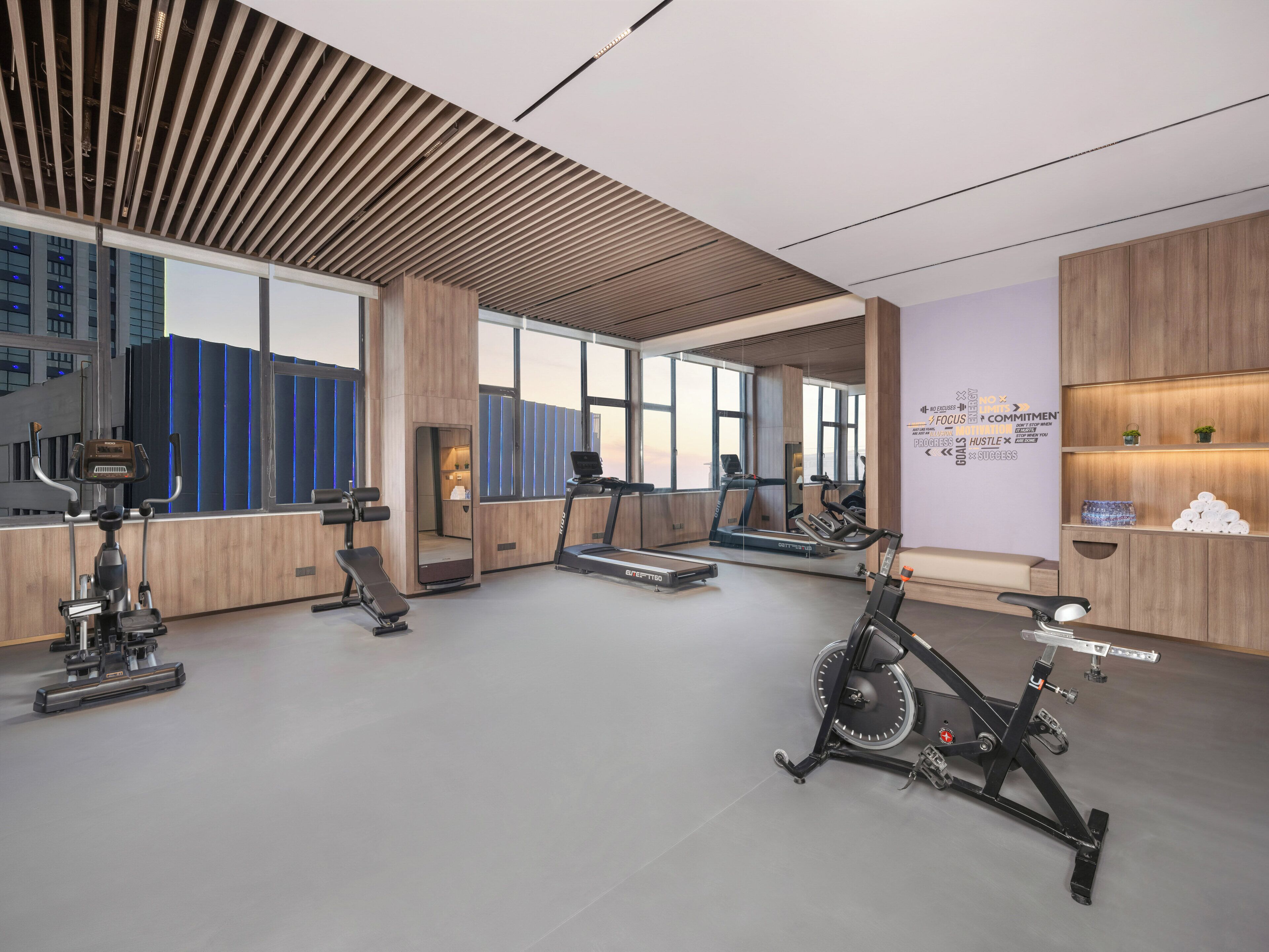 A modern gym with exercise equipment, large windows, and motivational wall art.