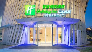 A Holiday Inn Express hotel entrance with a modern design, featuring a prominent green logo and signage in both English and Chinese.