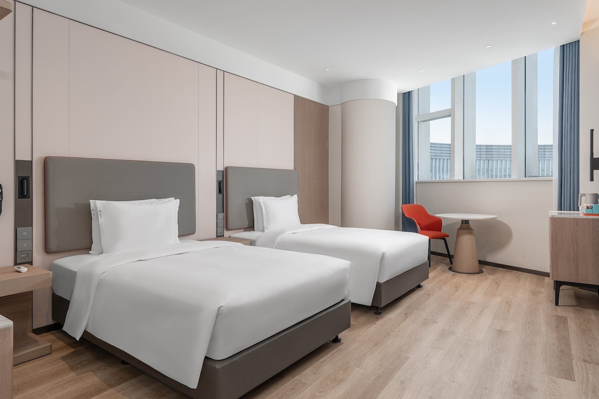 Una habitación de hotel moderna con dos camas, un escritorio, una silla y un televisor grande.