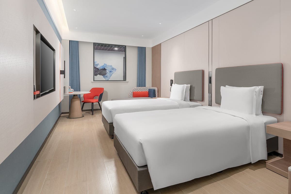 Una habitación de hotel moderna con dos camas, un escritorio, una silla y un ventanal grande.