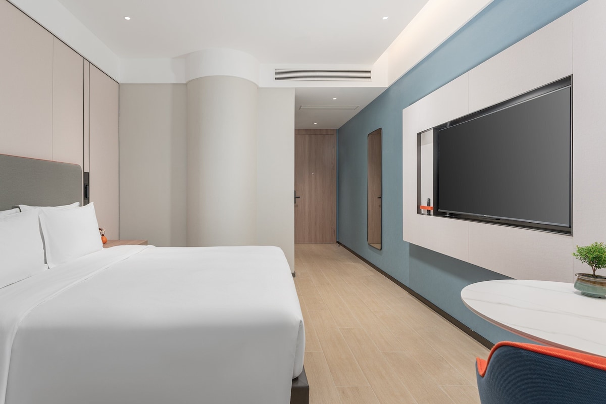 Una habitación de hotel moderna con una cama grande, un escritorio, una silla y un televisor fijado a la pared.