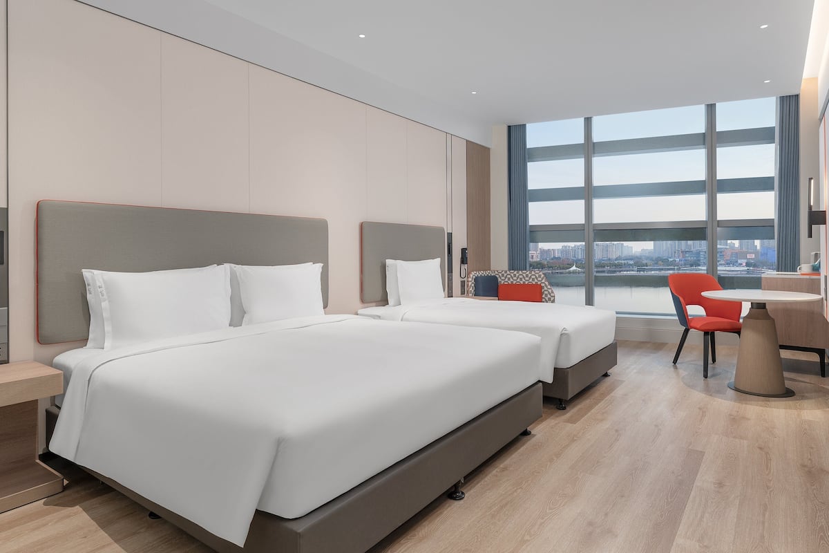 Una habitación de hotel moderna con dos camas, un escritorio y un gran ventanal con vistas a la ciudad.
