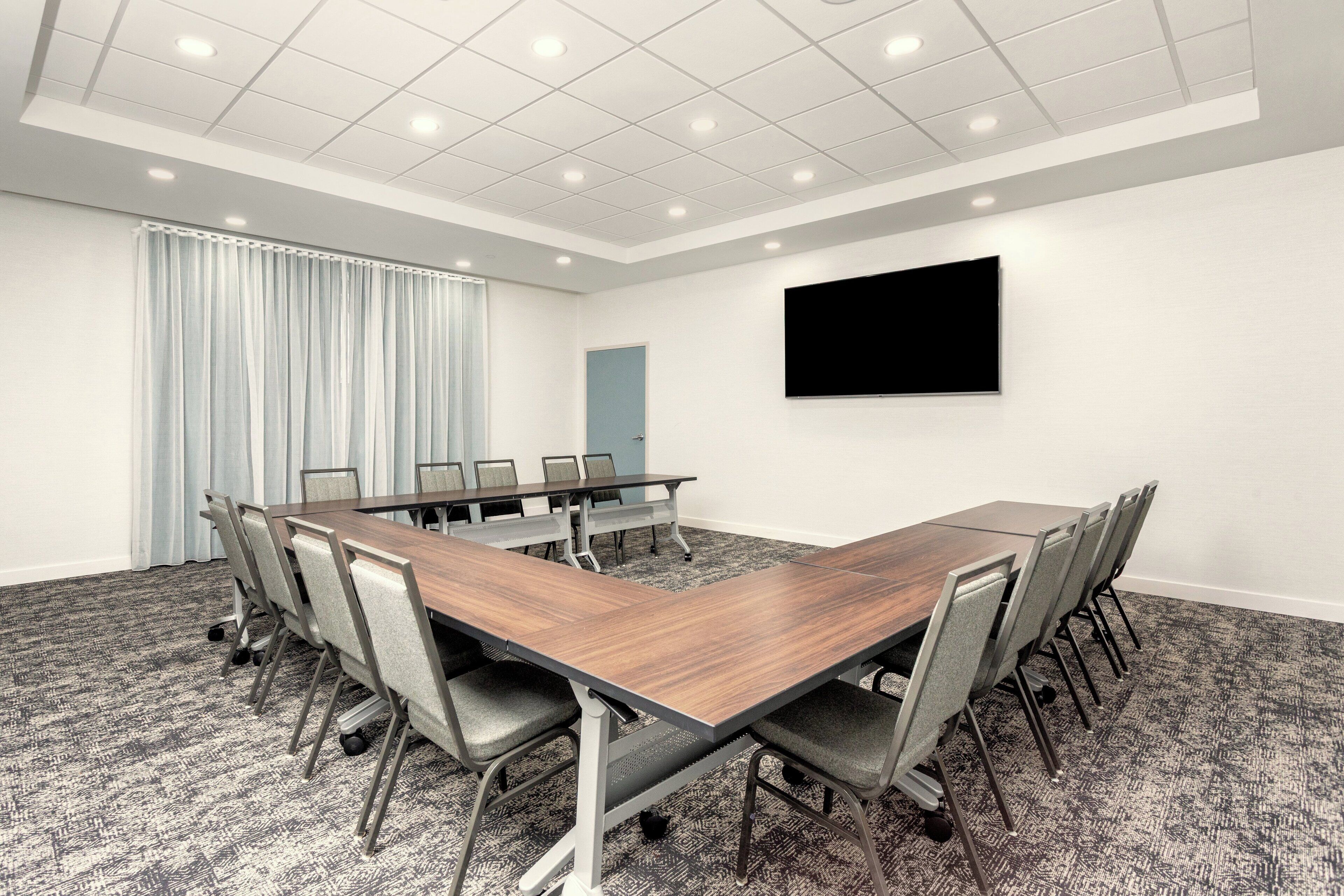 A conference room with a long table, chairs, a flat-screen TV, and a door.