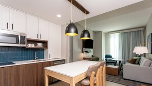 Une cuisine moderne équipée d’un four à micro-ondes, d’un évier et de meubles en bois. On y trouve également un coin repas avec une table et des chaises. Le salon est aménagé avec un canapé et une lampe.