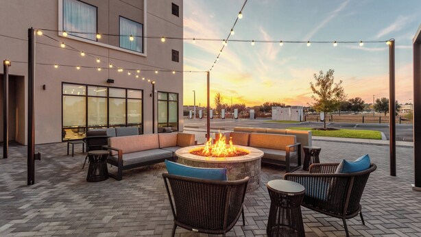 Un espace extérieur aménagé avec des sièges, un foyer, des meubles en osier et des guirlandes lumineuses, le tout sur fond de coucher de soleil.