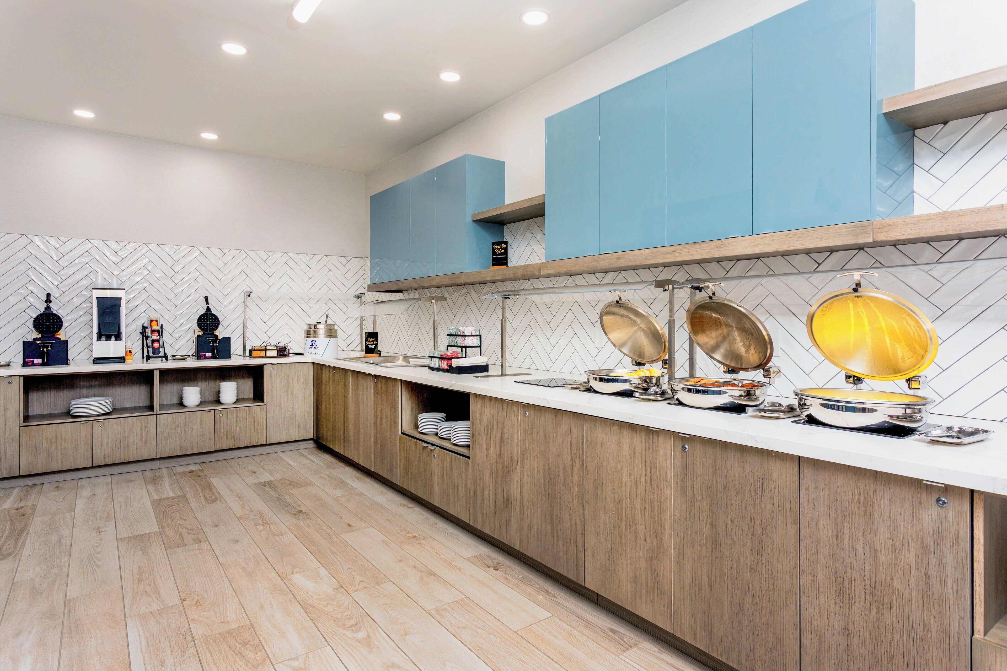 Une cuisine moderne avec des meubles en bois, un plan de travail blanc et un dosseret en carreaux disposés en motif chevron.