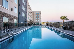 Una piscina con muro in pietra e ringhiere metalliche, circondata da un edificio con numerose finestre e una facciata in pietra.