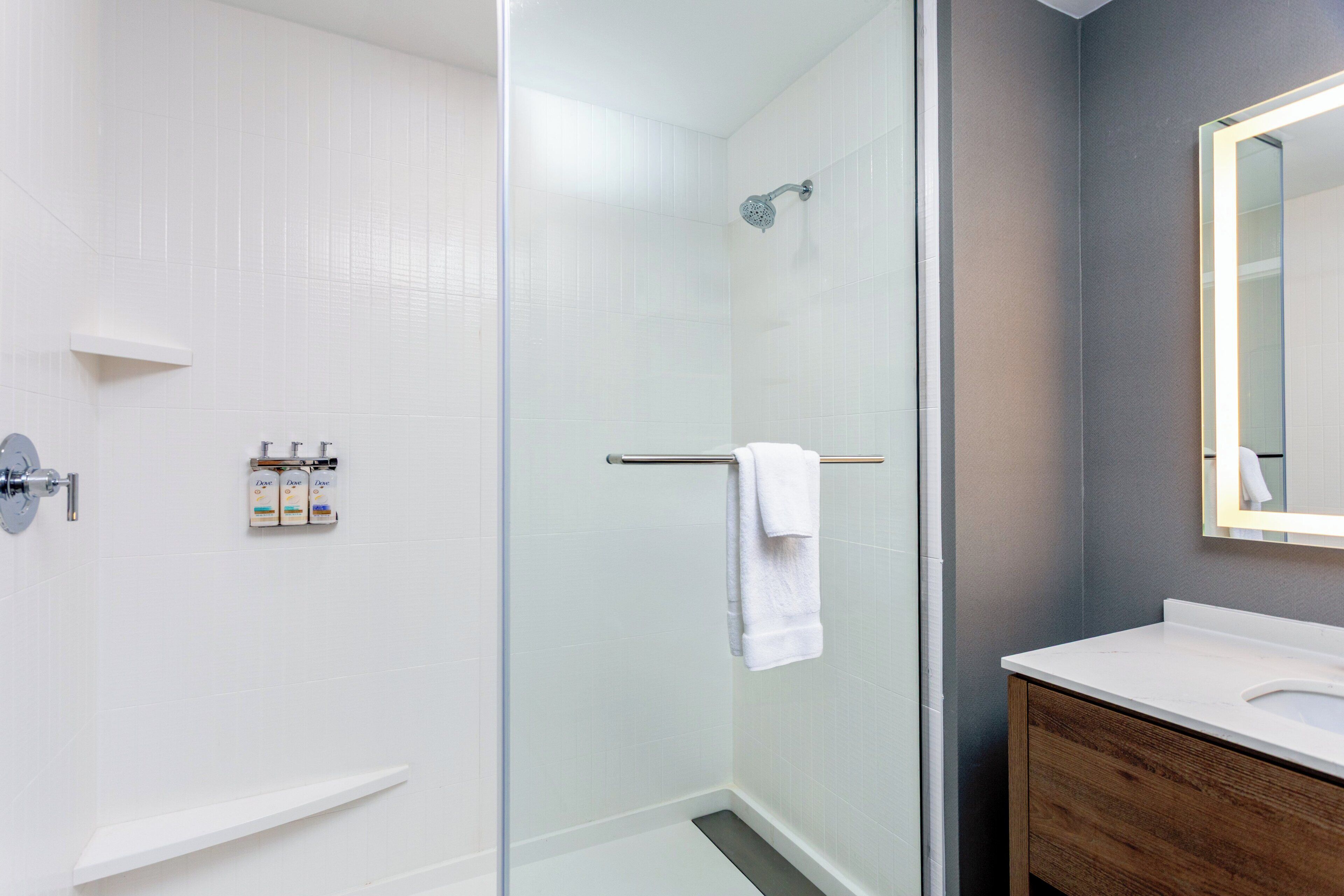 Un baño moderno con cabina de ducha de vidrio, lavamanos blanco y mueble de tocador de madera.