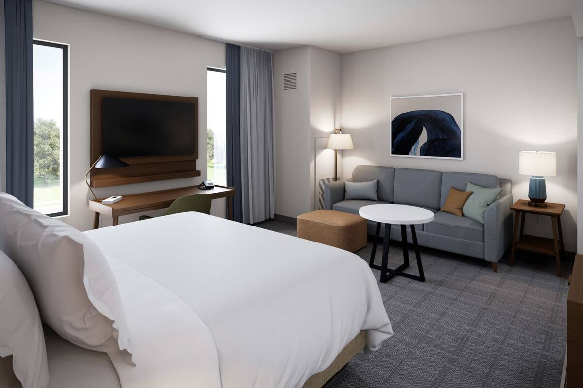 A hotel room with a large bed, a sofa, a small round table, a TV, and a painting on the wall.