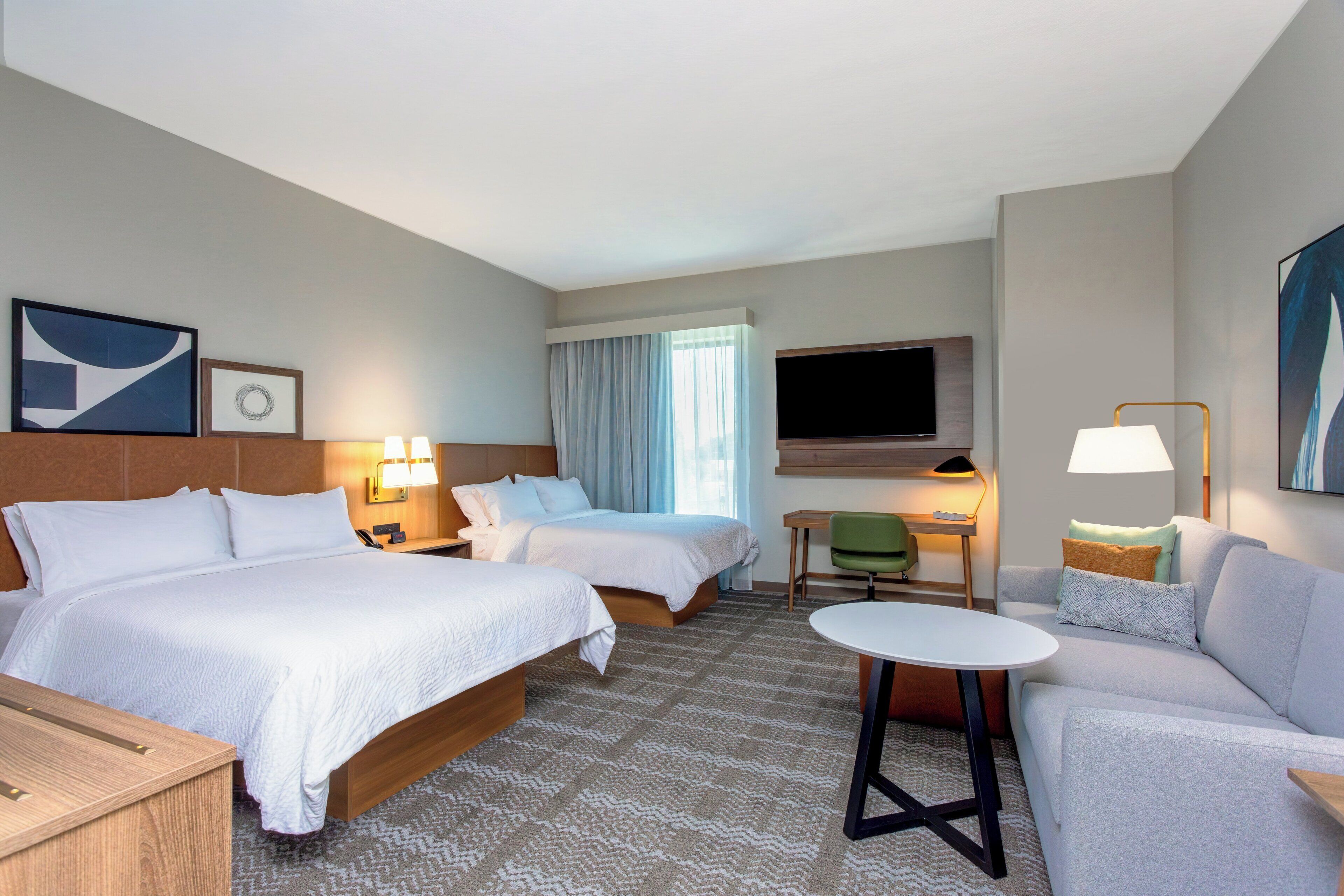 A hotel room with two beds, a sofa, a TV, and a desk with a chair.