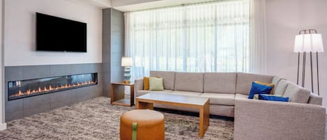 A modern living room with a flat-screen TV, a fireplace, a sofa, a coffee table, and a floor lamp.