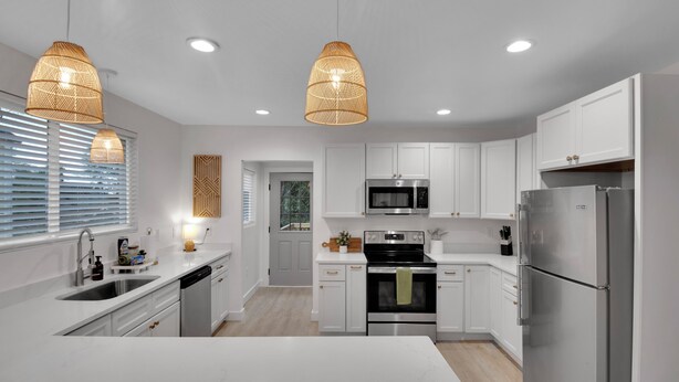 Una cocina moderna con armarios blancos, electrodomésticos de acero inoxidable e iluminación colgante.