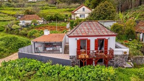 Ein weißes Gebäude mit rotem Dach und Balkon, umgeben von üppiger Vegetation und weiteren Häusern.