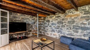 Ein rustikaler Raum mit Steinsandsteinwänden, Holzbalkendecke, einem Flachbildfernseher, einem kleinen Tisch mit einer Schüssel und einem blauen Sofa.