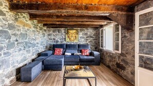 Ein gemütlicher Raum mit einer Steinwand, einem dunkelblauen Sofa mit roten Kissen, einem Holztisch und einer Buddha-Statue.