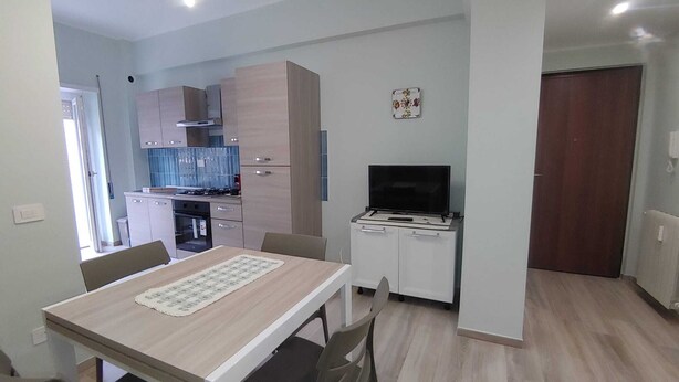 Une cuisine compacte dotée d’appareils électroménagers modernes, un coin repas avec une table et des chaises, et un petit téléviseur posé sur un meuble.