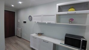 Une pièce avec un meuble blanc, un four à micro-ondes et une petite étagère ornée d’objets décoratifs.