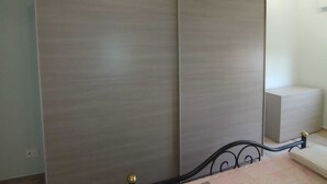 Une chambre avec une grande armoire, un lit avec un cadre en métal et une petite table de chevet.