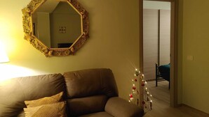 Un salon avec un canapé en cuir marron, un miroir décoratif et un petit sapin de Noël illuminé.