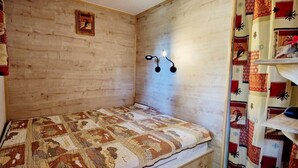 A small, cozy room with a wooden headboard, a patterned quilt on the bed, and a shelf with a decorative item. - 200m from ski slopes, 1st floor, balcony, tv, 26m², Montalbert (La Plagne)