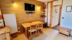 A small, cozy kitchen with a wooden table and chairs, a TV mounted on the wall, and a refrigerator. - 200m from ski slopes, 1st floor, balcony, tv, 26m², Montalbert (La Plagne)