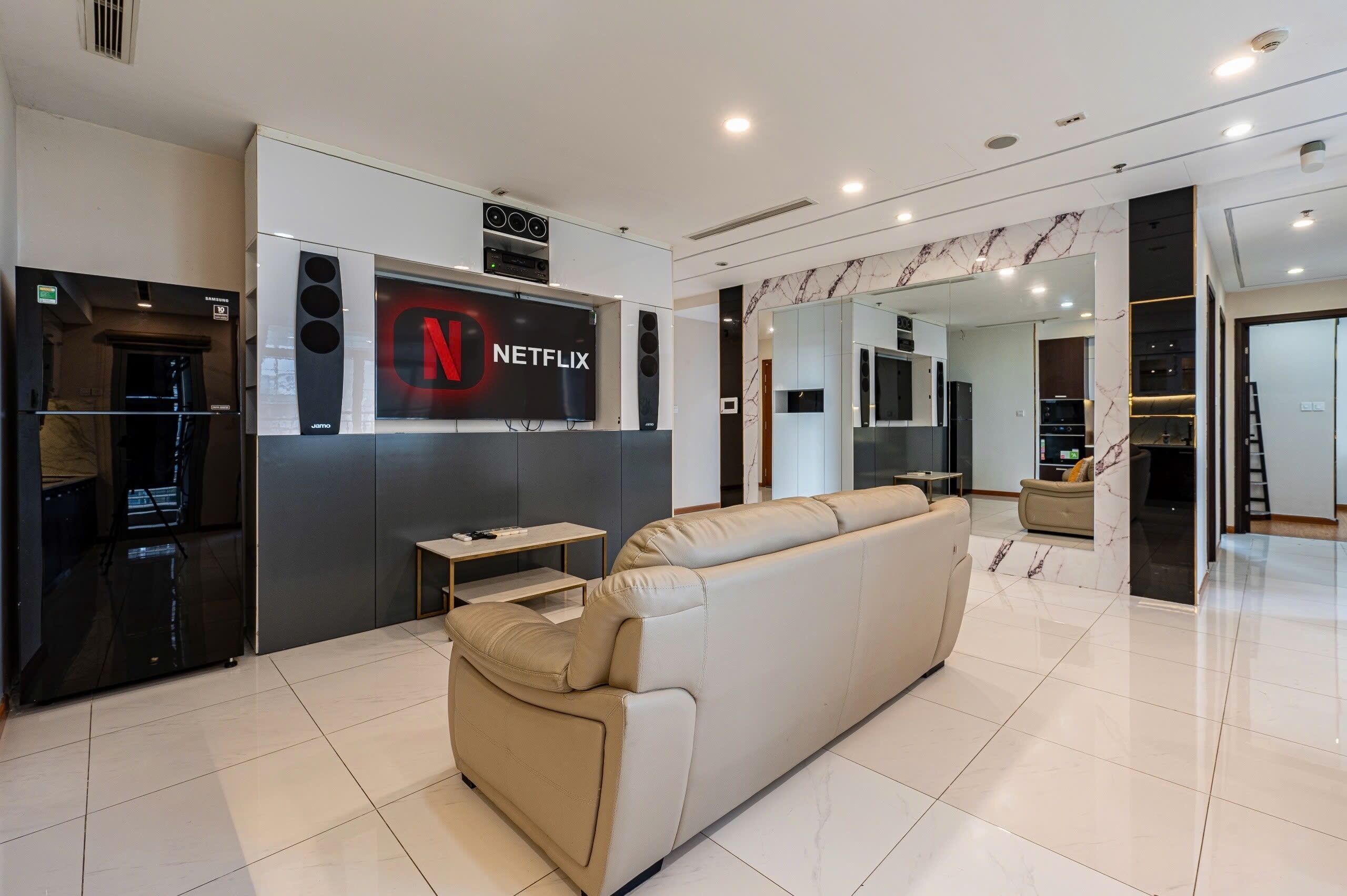 A modern living room with a beige sofa, a black entertainment unit, and a large Netflix logo on the wall.