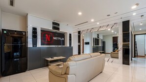 A modern living room with a beige sofa, a black entertainment unit, and a large Netflix logo on the wall. - 4 Bedroom Apartment for Rent at Vinhomes Central Park (Binh Thanh District)