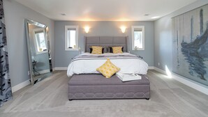 Un dormitorio moderno con una cama grande, lámparas de noche, un espejo y un cuadro en la pared.