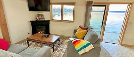 A living room with a fireplace, a sofa, a coffee table, and a view of the sea through large windows.