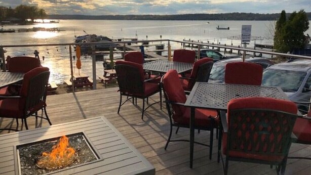An outdoor deck with tables and chairs, a fire pit, and a view of a body of water. - Lakefront Views + Walk to Dining | Kayaks + Firepit (Pewaukee)