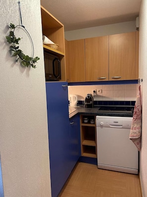 Een kleine keuken met houten kastjes, een witte vaatwasser, een fornuis en een magnetron.
