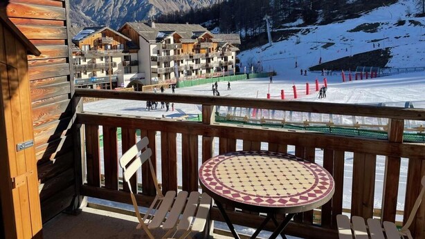 Een houten terras met een tafel en stoelen, met uitzicht op een piste en gebouwen op de achtergrond.