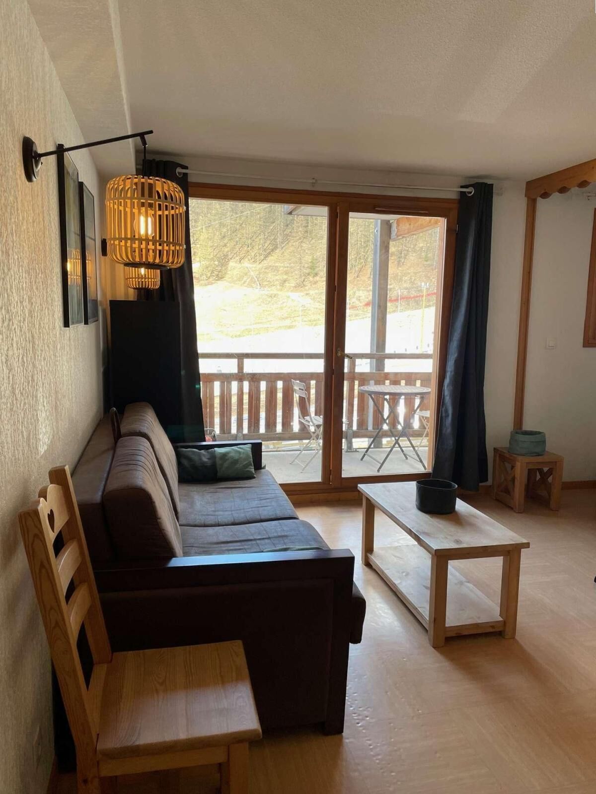 A cozy room with a sofa, a wooden table, and a bench. There is a large window with a view of the outdoors.