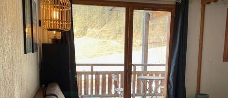 A cozy room with a sofa, a wooden table, and a bench. There is a large window with a view of the outdoors.
