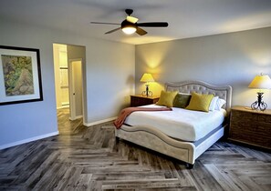 A bedroom with a bed, two bedside tables, a ceiling fan, and a door leading to another room. - Estrella Skies Backyard Delight, Stunning Pool 4 Beds 2 Bath, Vacation Retreat (Goodyear)